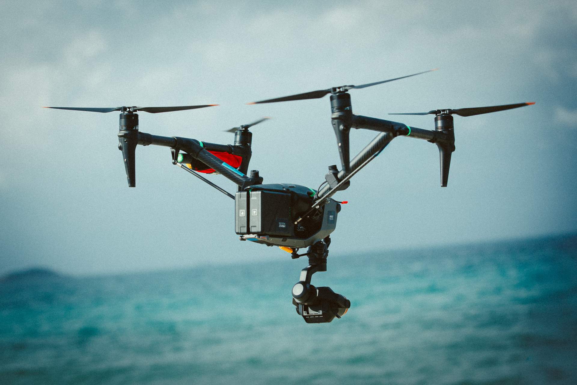 Drone en vol stationnaire au-dessus de la mer, caméra sous nacelle orientée vers le bas.